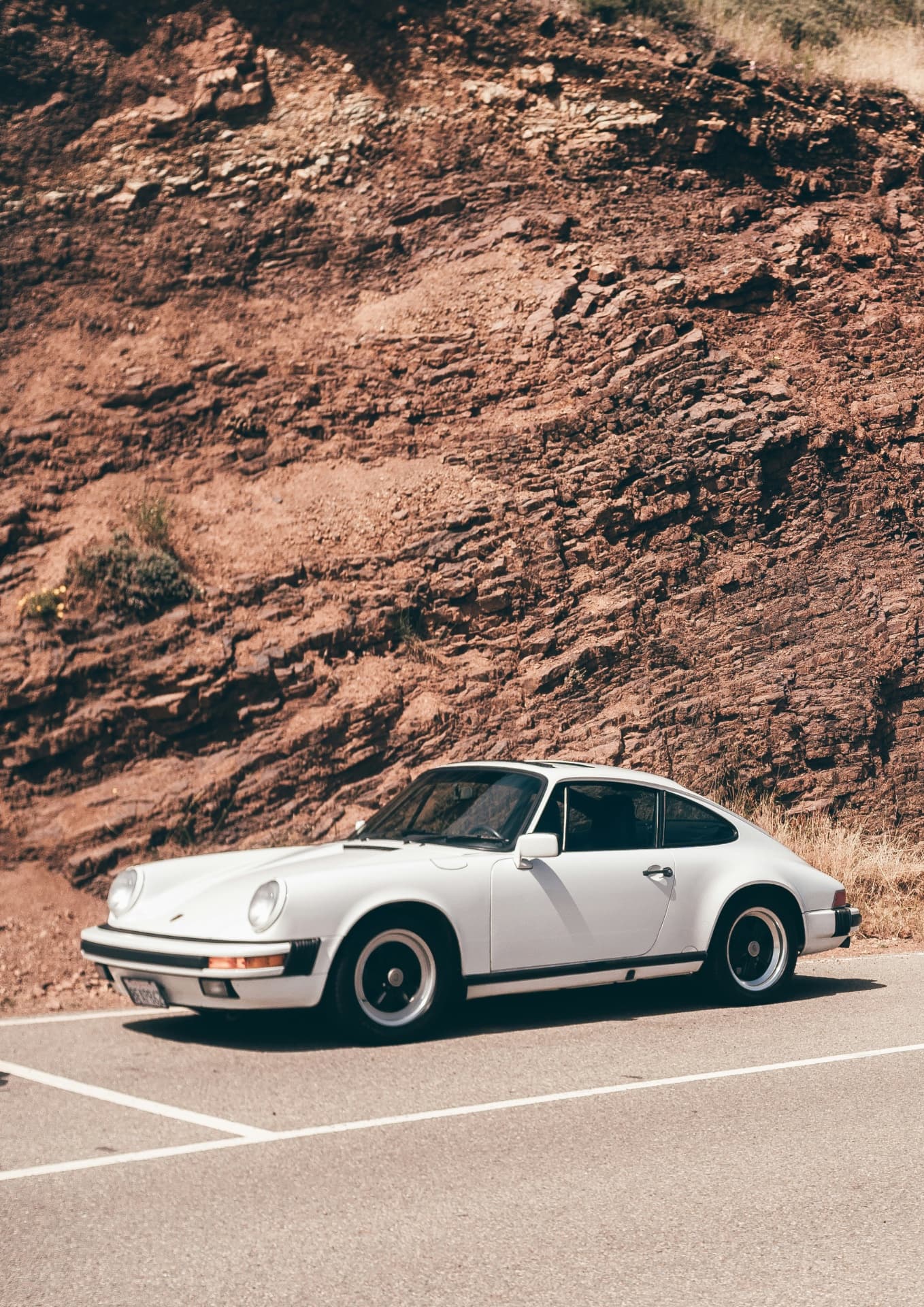 Белый классический Porsche припаркован у скалистых гор на асфальтированной дороге