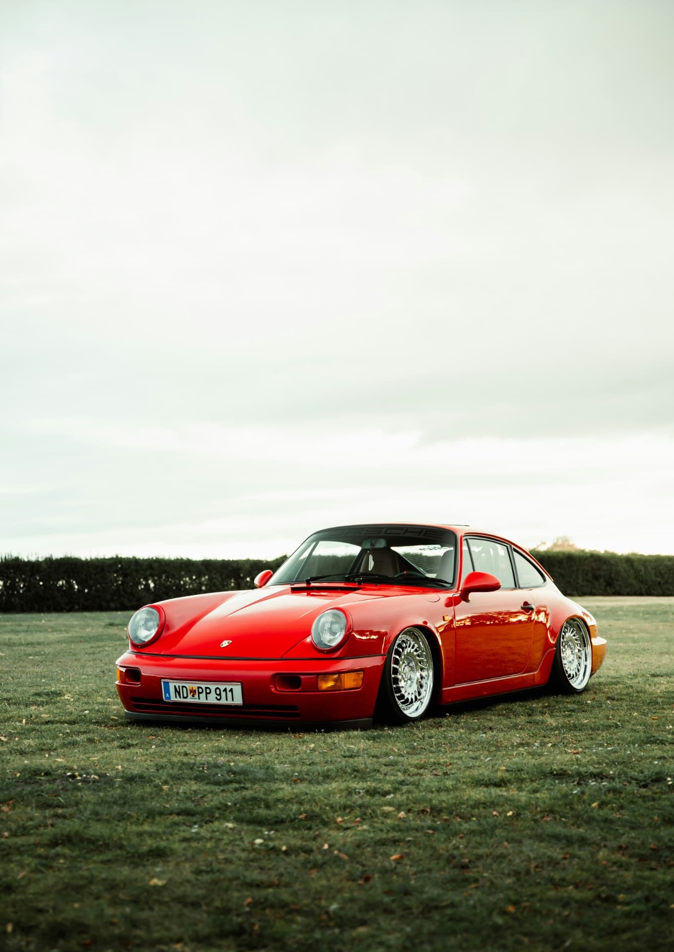 Красный Porsche 911 на фоне зелёного поля и неба