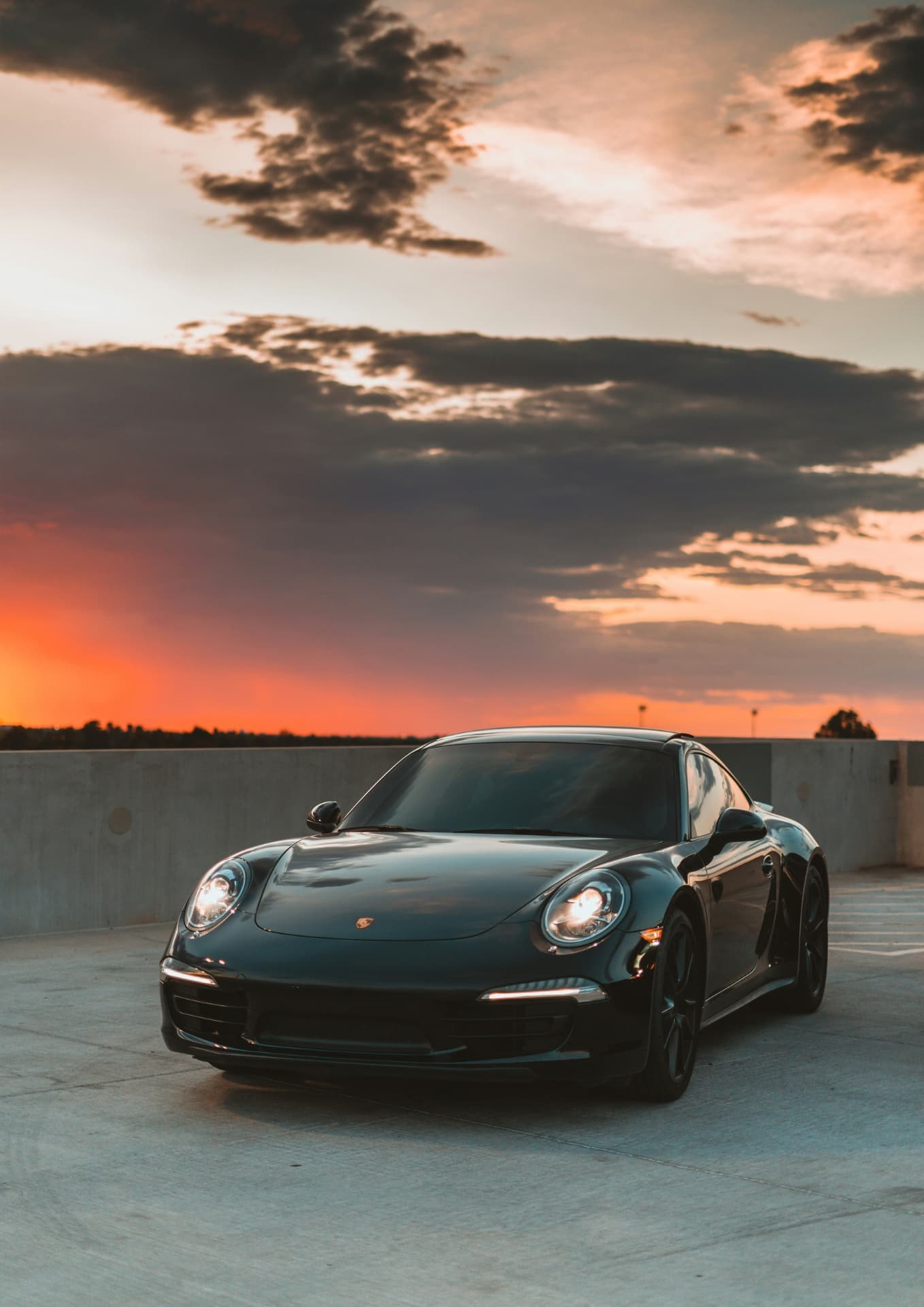 Чёрный Porsche 911 припаркован на фоне драматического закатного неба с облаками