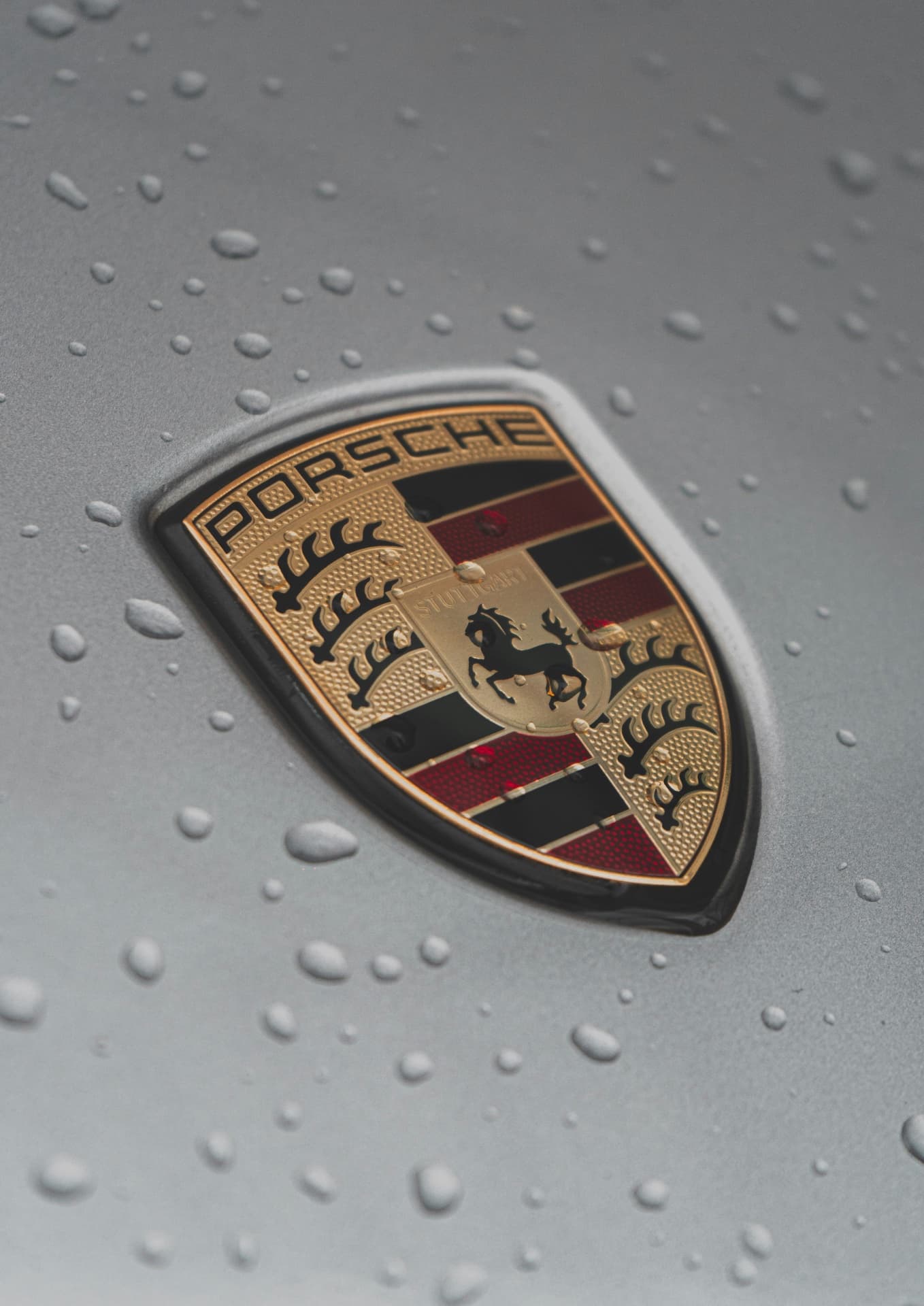 Золотая эмблема Porsche с черным конем на сером фоне с каплями воды